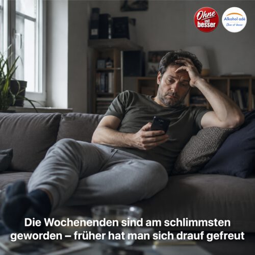 Ein Mann sitzt allein erschöpft auf einem Sofa in seiner Wohnung und blickt mit müdem, genervtem Ausdruck auf sein Smartphone. Das gedämpfte Tageslicht und die ruhige, etwas trostlose Atmosphäre vermitteln das Gefühl von Leere und Antriebslosigkeit, wie sie viele Menschen in der frühen Abstinenz besonders an Wochenenden erleben.